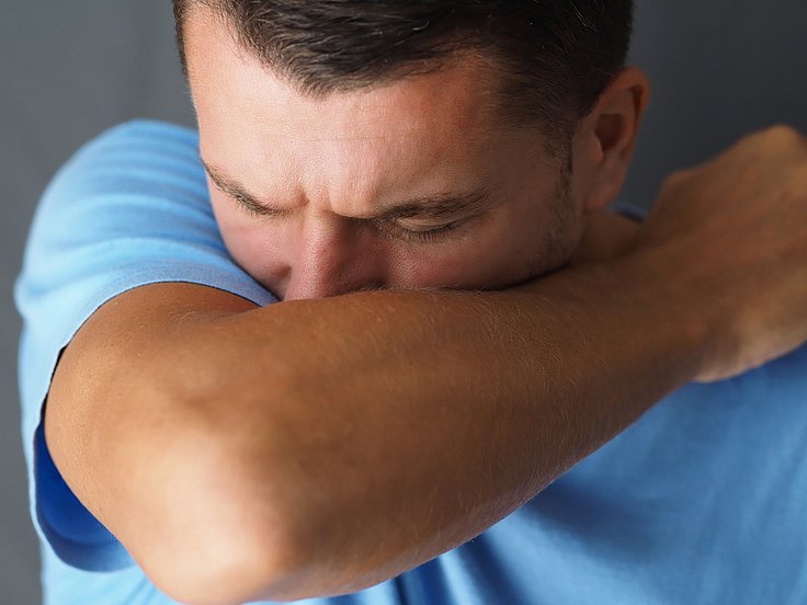 Ein Mann mit einer Erkältung hustet in die Armbeuge. © dreii/ shutterstock.com